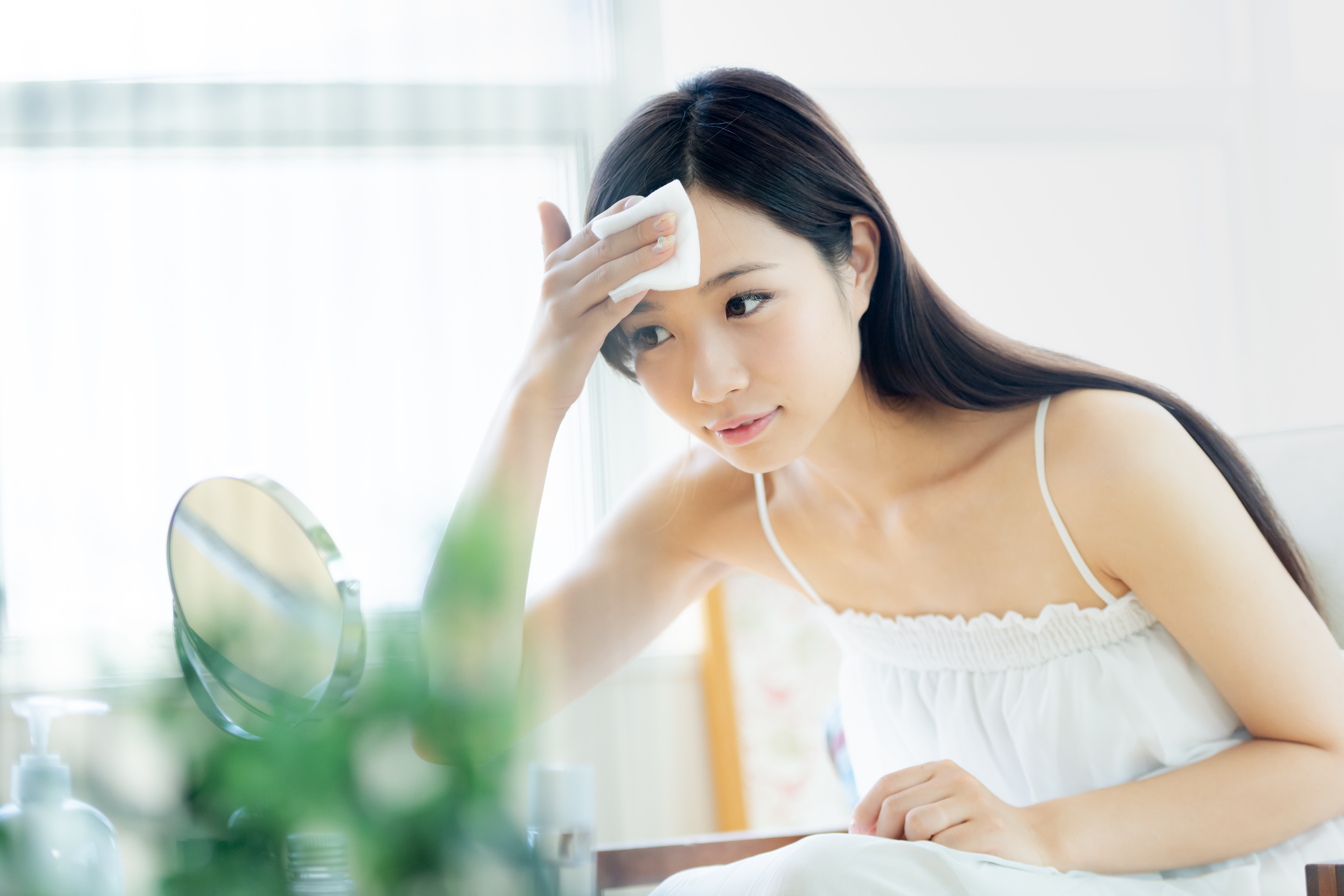 鏡の前でコットンを手に持ち、おでこや肌をやさしくお手入れする女性