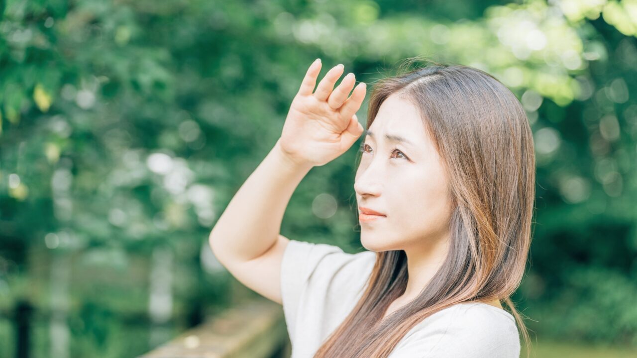 屋外で日差しを遮るように手をかざす女性