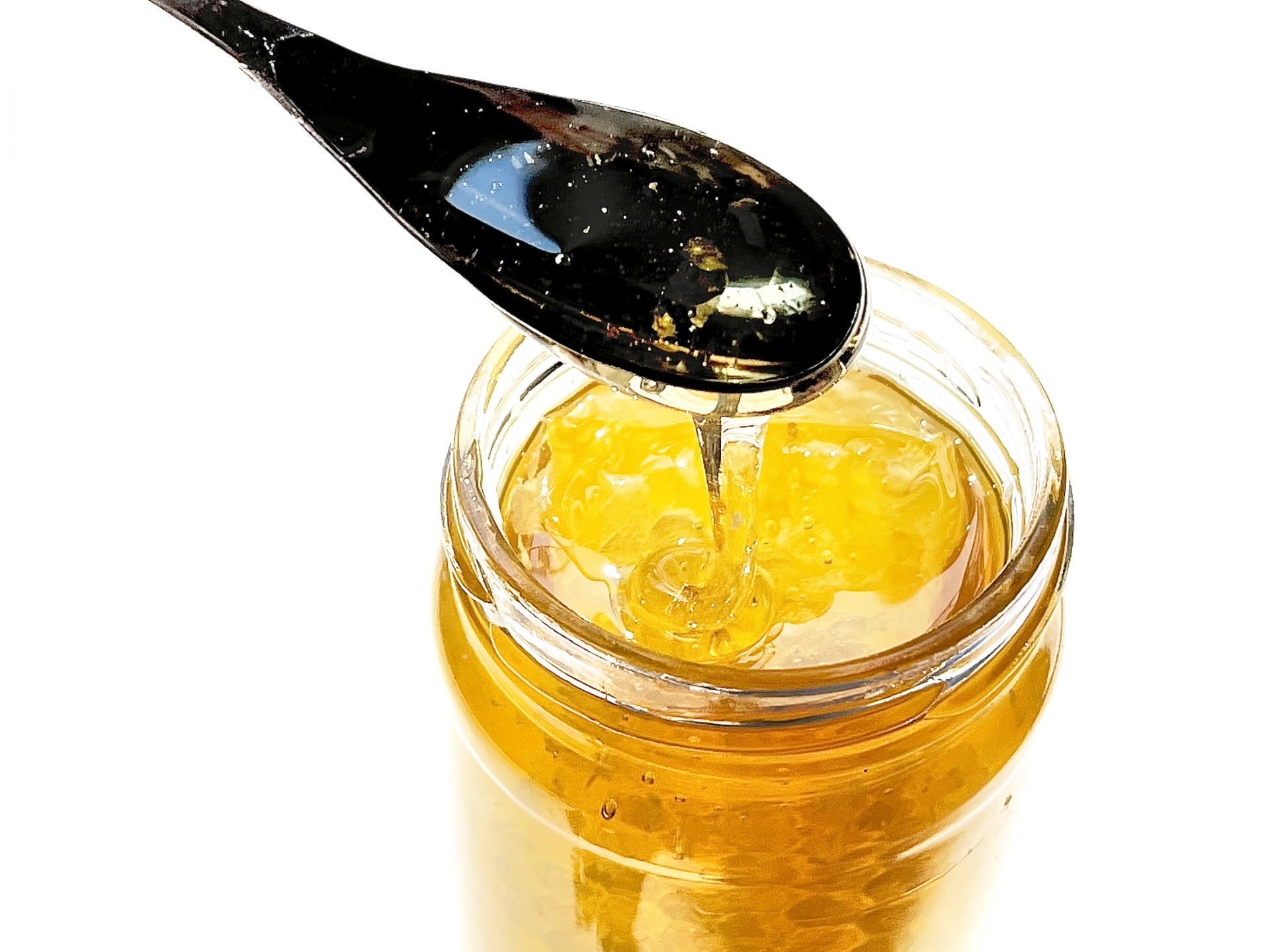 瓶からスプーンですくい上げた、透明感のある黄金色のはちみつ