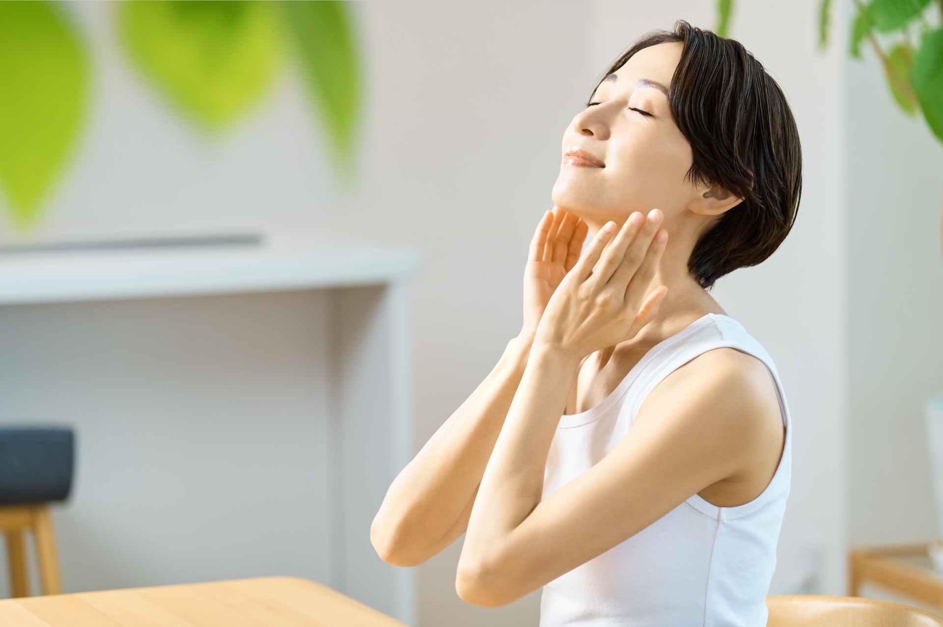 スキンケア後に満足そうな表情で、首筋から顎にかけて両手で優しく触れる女性