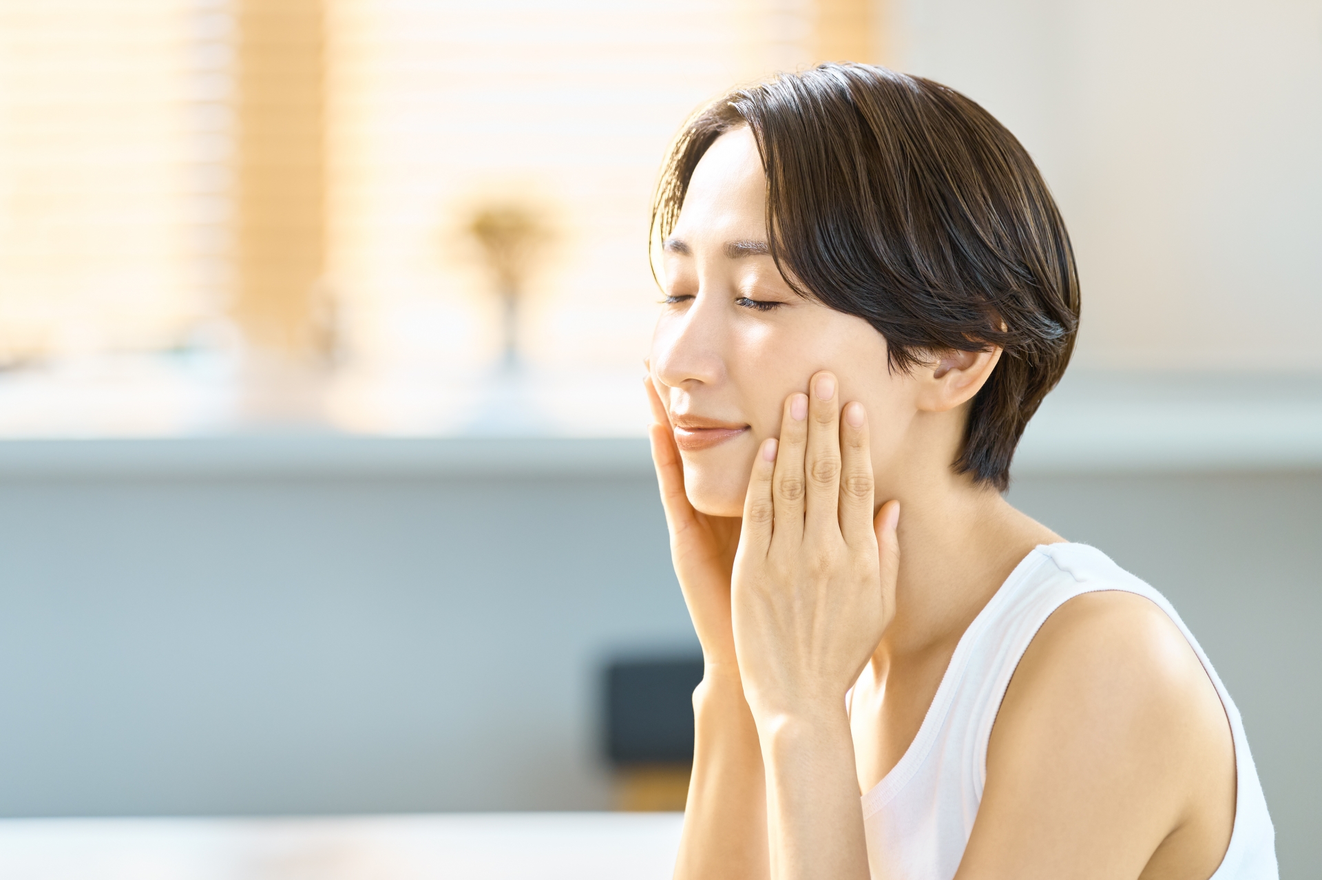 両手で優しく顔を包み込み、肌のお手入れをする女性の横顔