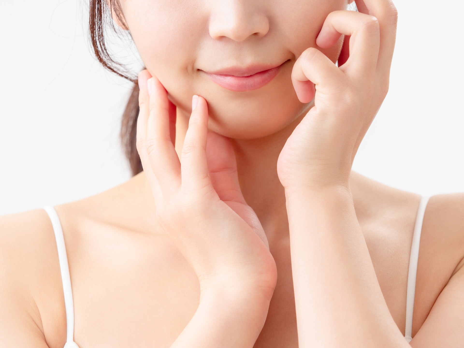 両手で自分の頬に優しく触れる女性。