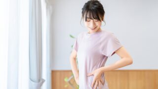 笑顔で自分のウエストに手を添える、トレーニングウェア姿の女性。基礎代謝や健康管理をイメージしたアイキャッチ画像。
