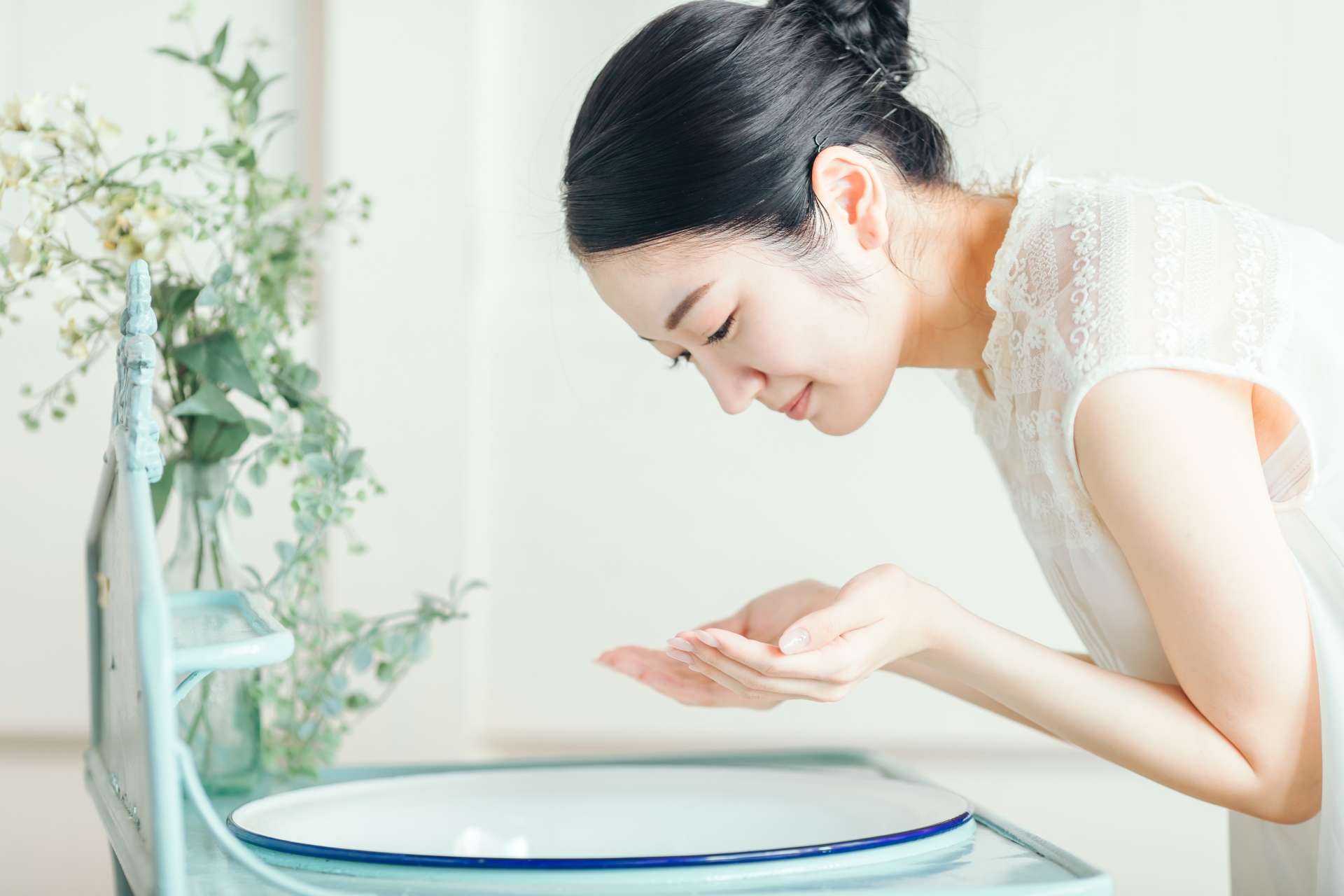 洗面台でぬるま湯を手に取り、優しく洗顔をする女性