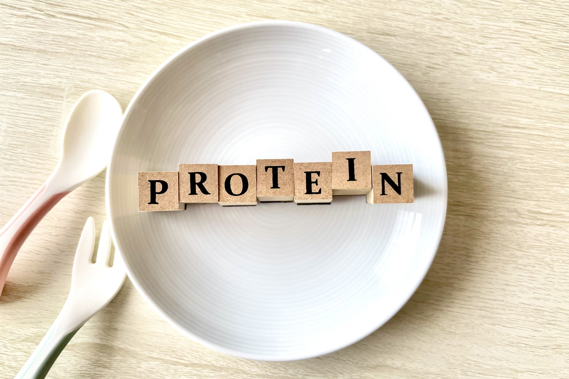 白い丸皿の上に「PROTEIN」と書かれたアルファベットのウッドブロックが並んでいる写真。