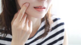 女性が、頬の赤みやポツポツを気にして指を添えている様子