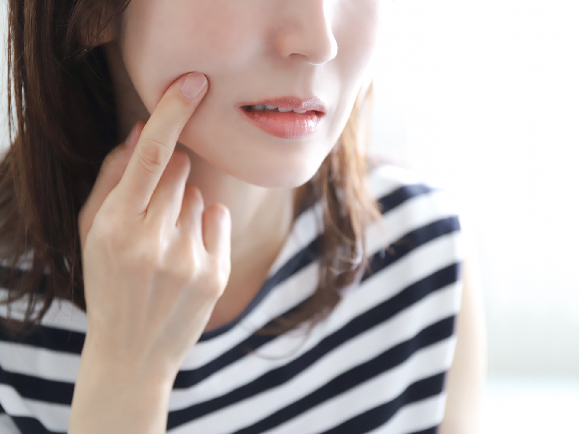 自分の指先で頬に触れながら肌荒れやバリア機能の低下を気にしているイメージ