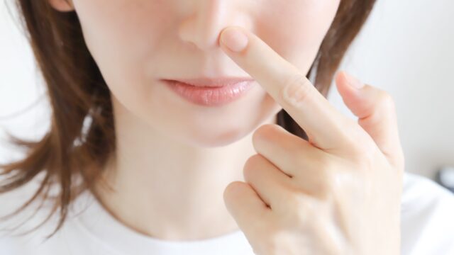 気になる鼻の黒ずみや毛穴汚れを指で指して確認している女性の顔のアップ。