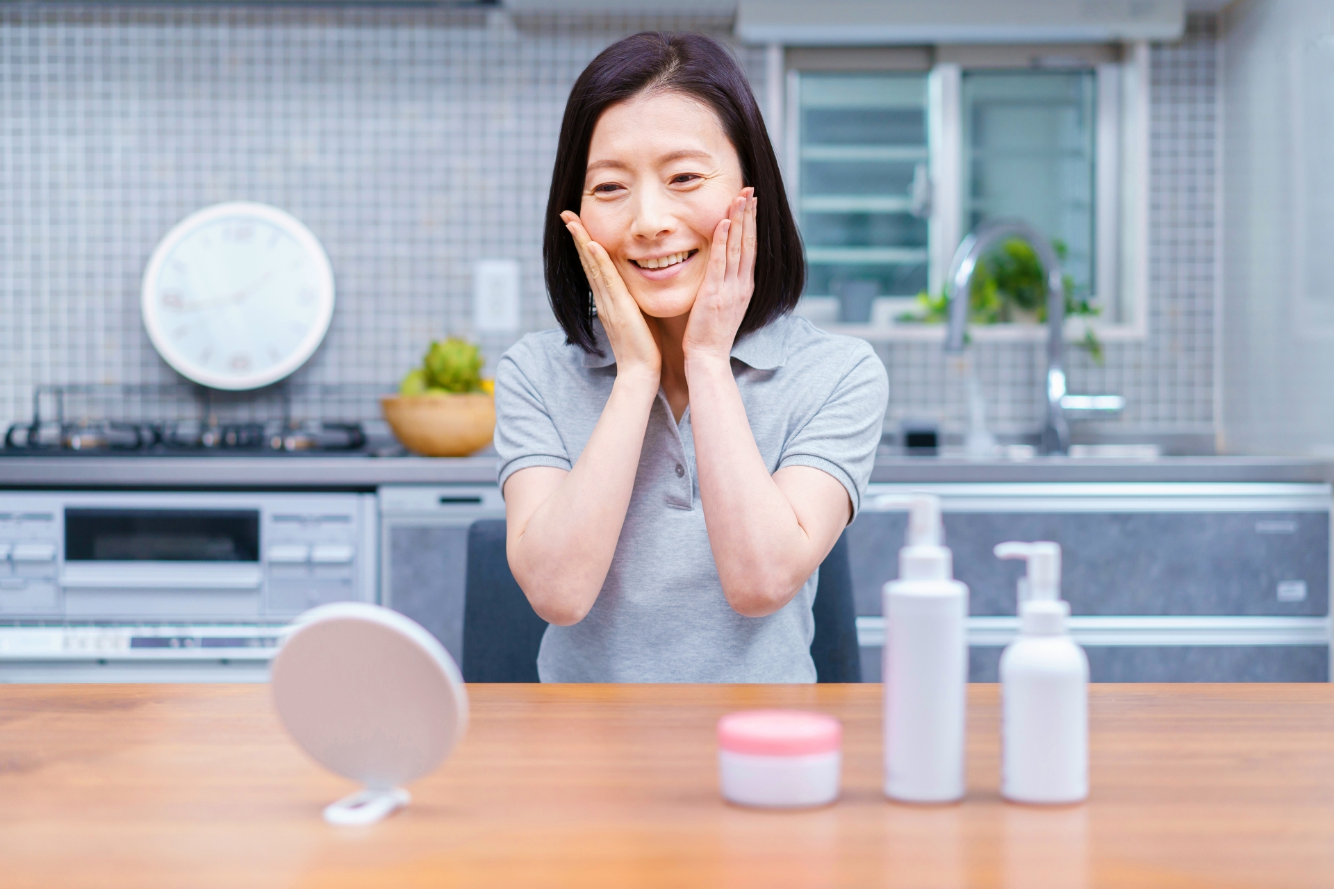 鏡の前で自分の両頬に手を添えて笑顔で肌状態を確認する女性