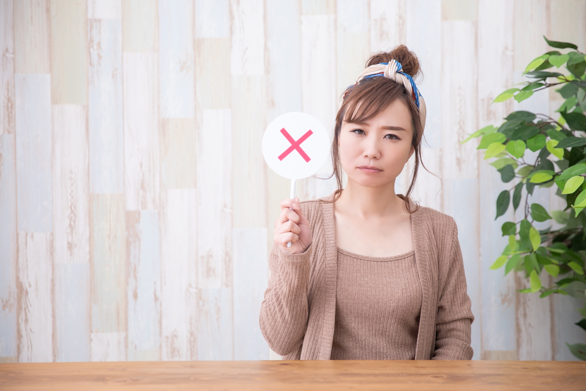 バツ印の札を掲げて困った表情をする女性