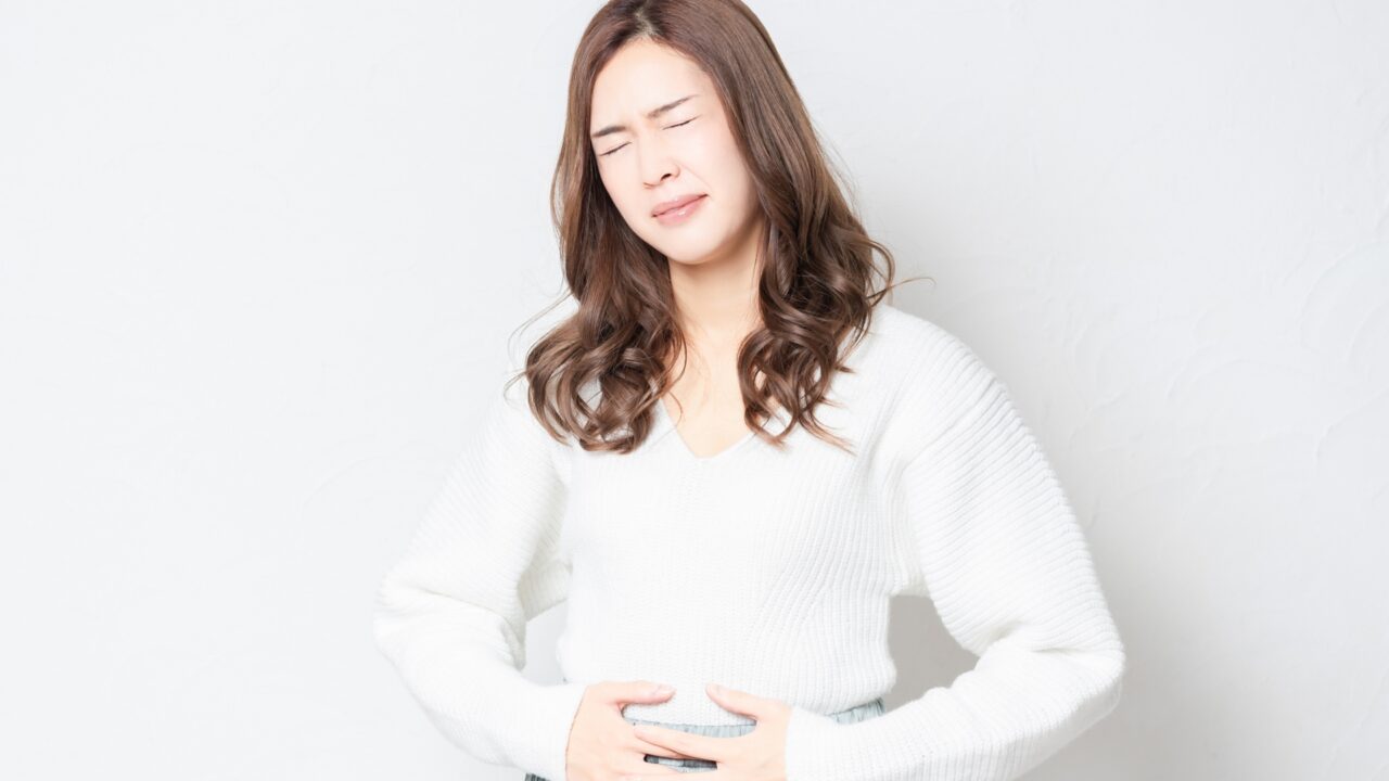 お腹を両手で押さえ、辛そうな表情で痛みに耐えている女性の写真。