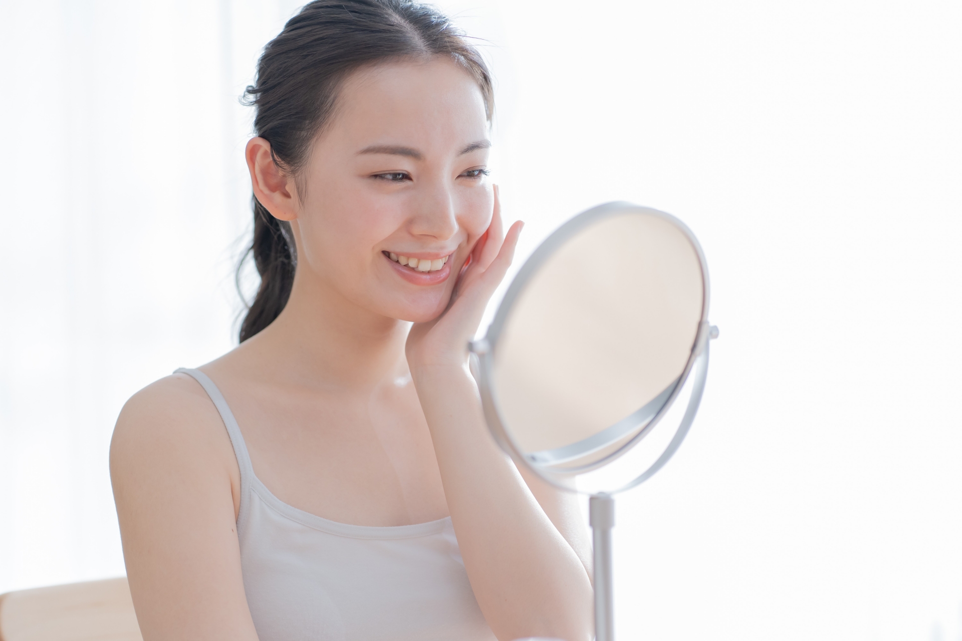 卓上鏡に向かい、片手を頬に添えて微笑む女性